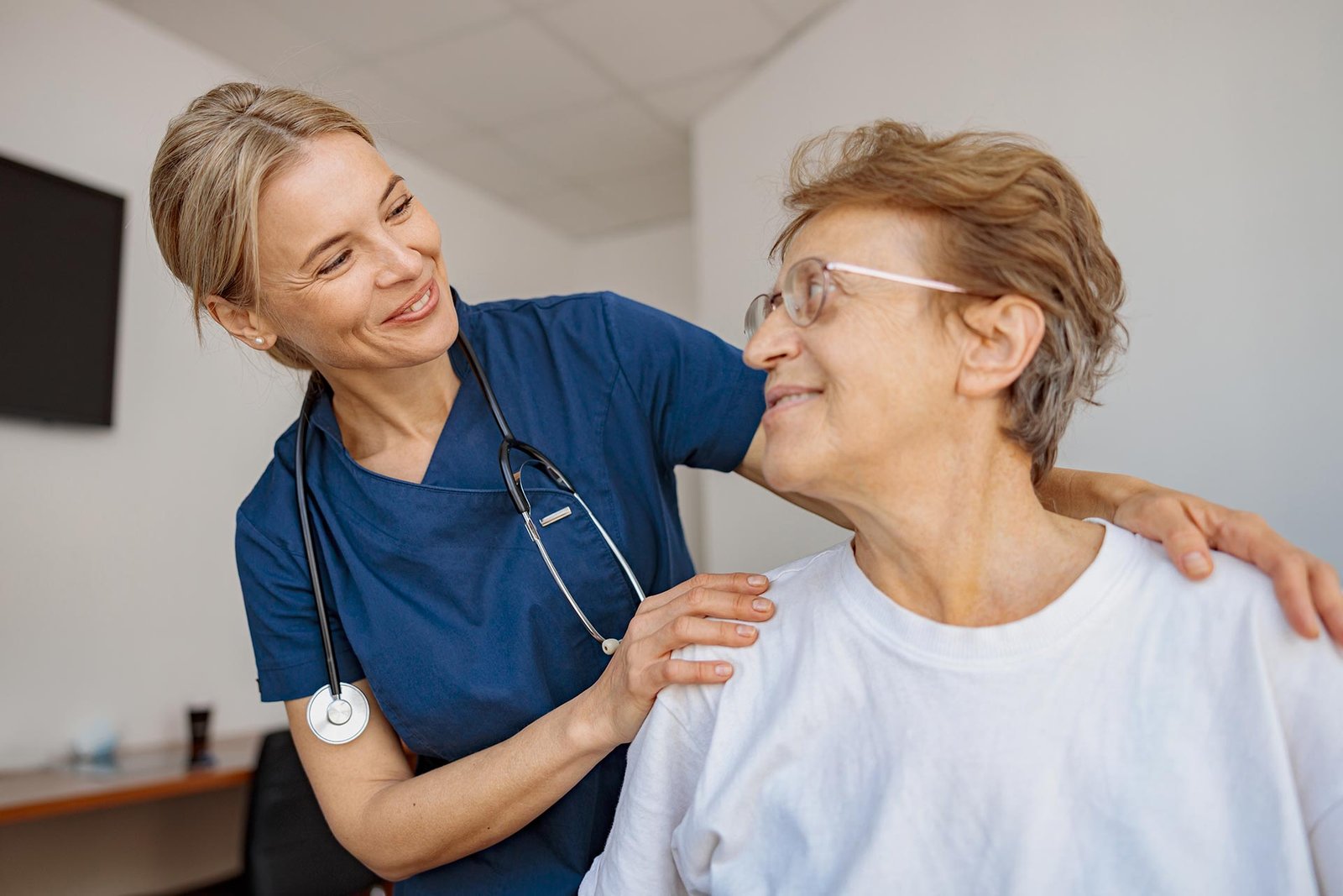 Nurse with a hand on the shoulder of an older woman patient